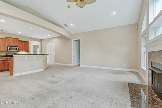 unfurnished living room with vaulted ceiling, a tiled fireplace, ceiling fan, and light carpet