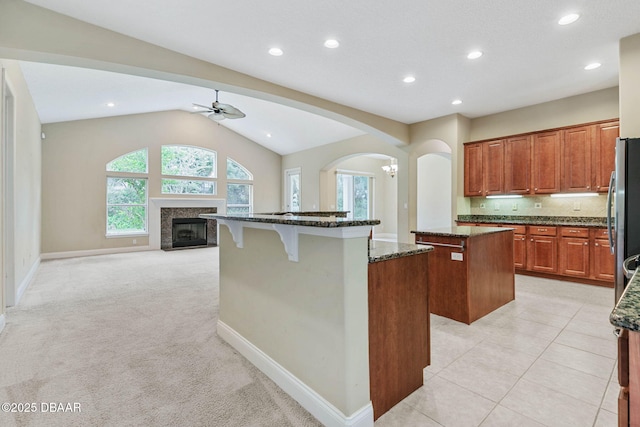 kitchen with a kitchen island, lofted ceiling, a high end fireplace, dark stone counters, and light carpet