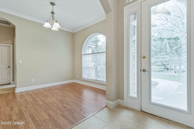 tiled foyer entrance with a chandelier and crown molding