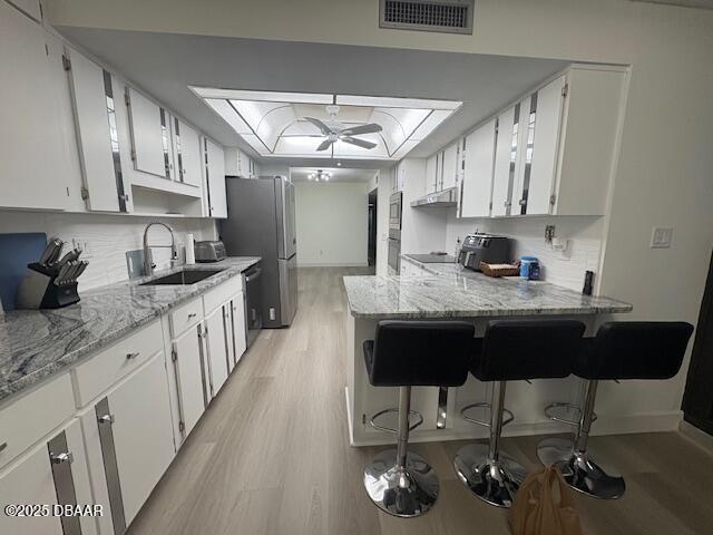 kitchen featuring a sink, light wood-type flooring, dishwashing machine, a ceiling fan, and a tray ceiling