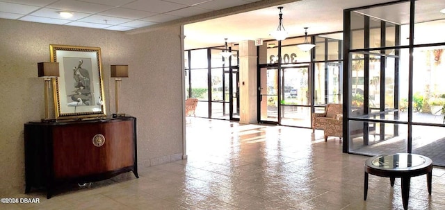 building lobby with floor to ceiling windows, a textured wall, and a drop ceiling