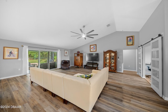 living room with a barn door, vaulted ceiling, ceiling fan, and wood-type flooring