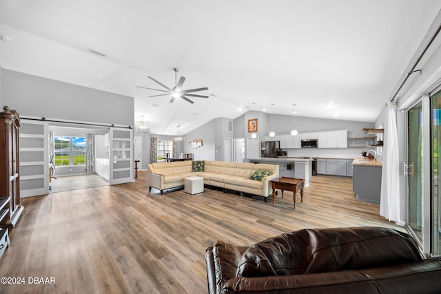 living room featuring light wood-type flooring, a barn door, high vaulted ceiling, sink, and ceiling fan