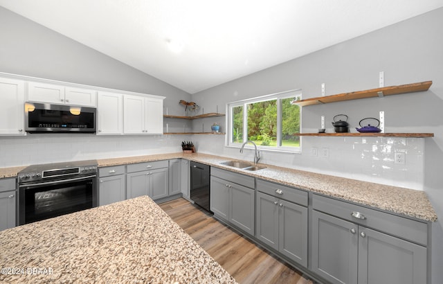 kitchen featuring stainless steel appliances, vaulted ceiling, sink, backsplash, and light wood-type flooring