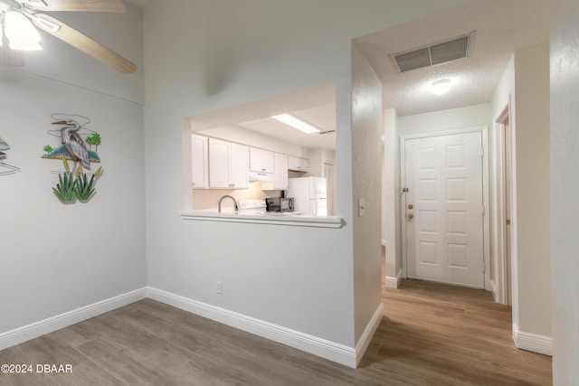 kitchen featuring hardwood / wood-style floors, white refrigerator, ceiling fan, a textured ceiling, and white cabinetry