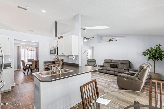 kitchen featuring wood finished floors, a peninsula, a sink, stainless steel appliances, and white cabinetry