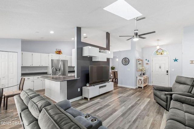 living area featuring a ceiling fan, baseboards, light wood finished floors, a skylight, and recessed lighting