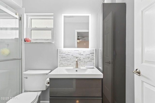 bathroom featuring tasteful backsplash, toilet, vanity, and a shower with door