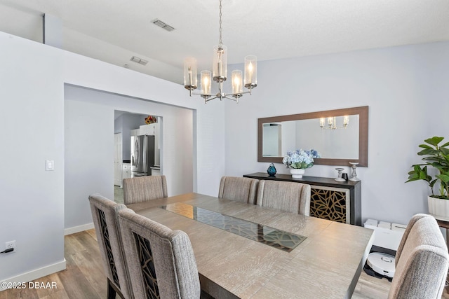 dining space with baseboards, light wood-style floors, visible vents, and a chandelier