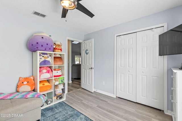 game room featuring visible vents, light wood-style flooring, a textured ceiling, baseboards, and ceiling fan