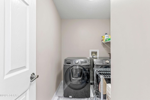 laundry area with tile patterned floors, washer and dryer, a textured ceiling, baseboards, and laundry area