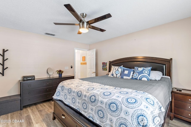 bedroom featuring a ceiling fan, visible vents, light wood finished floors, and a textured ceiling