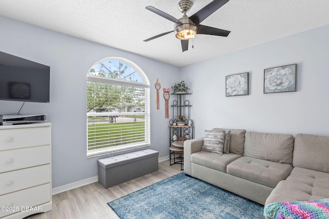 living area featuring baseboards, a textured ceiling, light wood-type flooring, and a ceiling fan