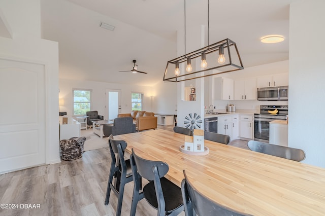 dining area featuring light hardwood / wood-style floors, ceiling fan, sink, and vaulted ceiling