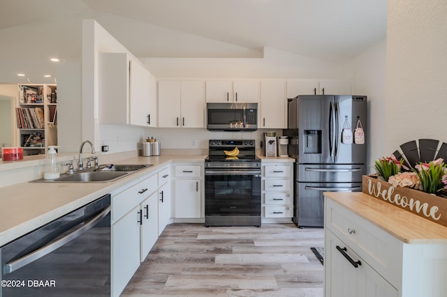 kitchen featuring sink, appliances with stainless steel finishes, light hardwood / wood-style flooring, white cabinets, and vaulted ceiling