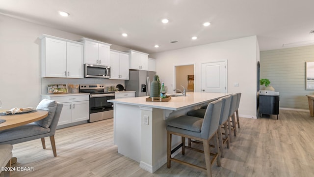 kitchen featuring a breakfast bar, stainless steel appliances, a kitchen island with sink, sink, and white cabinetry