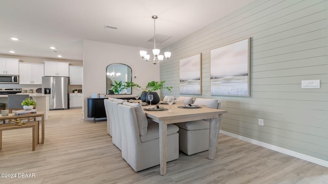 dining space with wood walls, light wood-type flooring, and an inviting chandelier