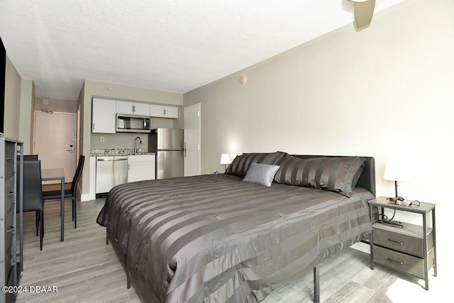 bedroom featuring stainless steel fridge, sink, light hardwood / wood-style floors, and a textured ceiling