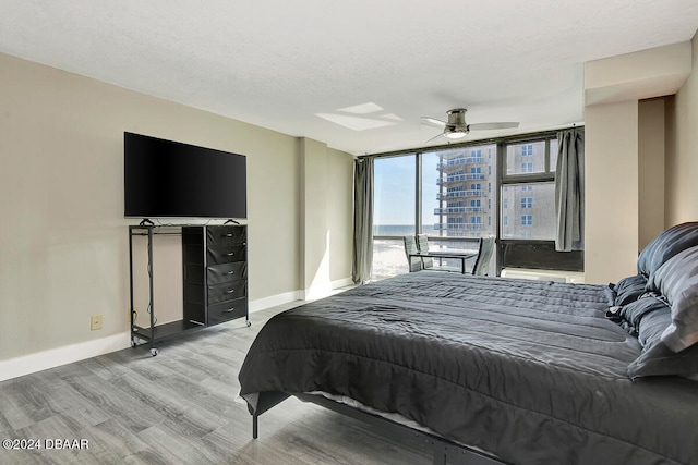 bedroom featuring ceiling fan, expansive windows, light hardwood / wood-style floors, and a textured ceiling