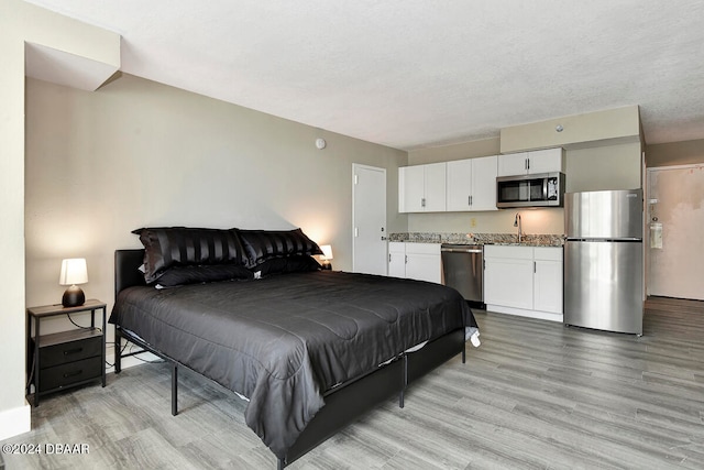 bedroom featuring stainless steel fridge, sink, light hardwood / wood-style floors, and a textured ceiling