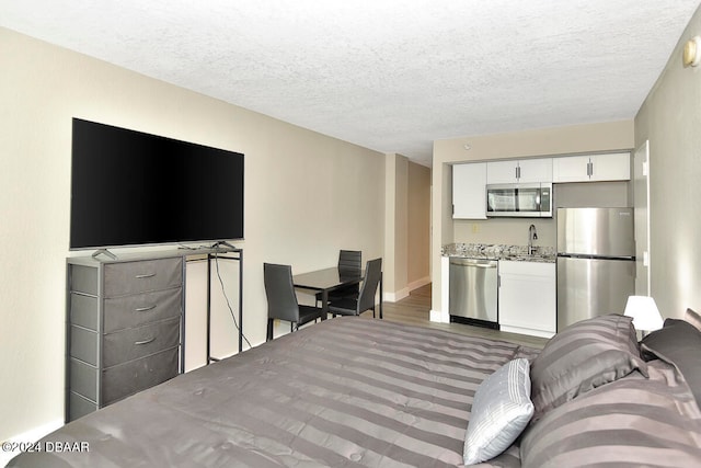 bedroom with stainless steel fridge, a textured ceiling, and sink