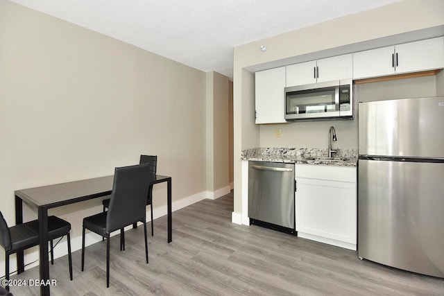 kitchen with stainless steel appliances, white cabinetry, and light hardwood / wood-style flooring