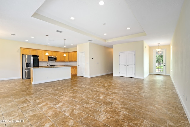 3651 Pini Ave, New Smyrna Beach, FL 32168 - kitchen with appliances with stainless steel finishes, decorative light fixtures, a tray ceiling, an island with sink, and decorative backsplash
