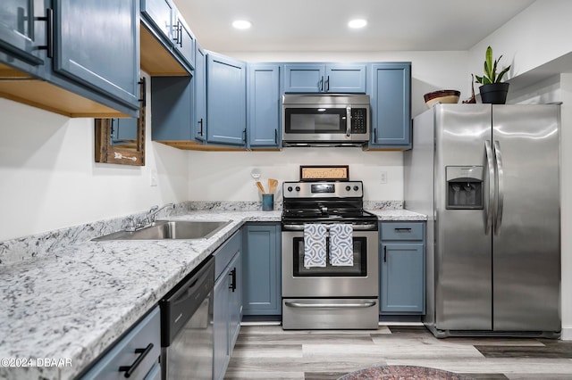 kitchen featuring stainless steel appliances, sink, light stone counters, light hardwood / wood-style flooring, and blue cabinets