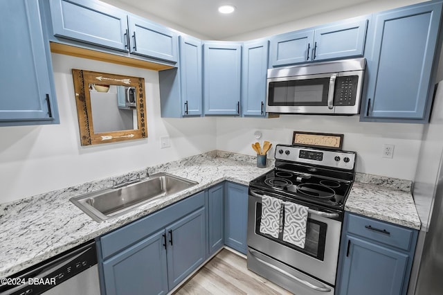 kitchen featuring stainless steel appliances, sink, blue cabinetry, light stone countertops, and light wood-type flooring