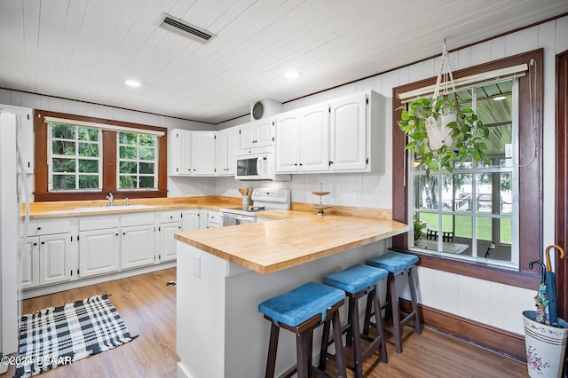 kitchen featuring light hardwood / wood-style floors, white cabinets, a breakfast bar area, sink, and white appliances