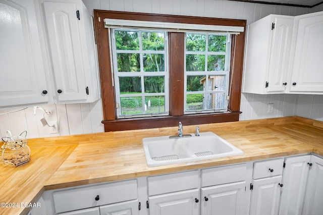 kitchen featuring white cabinetry, sink, tasteful backsplash, wooden walls, and butcher block countertops