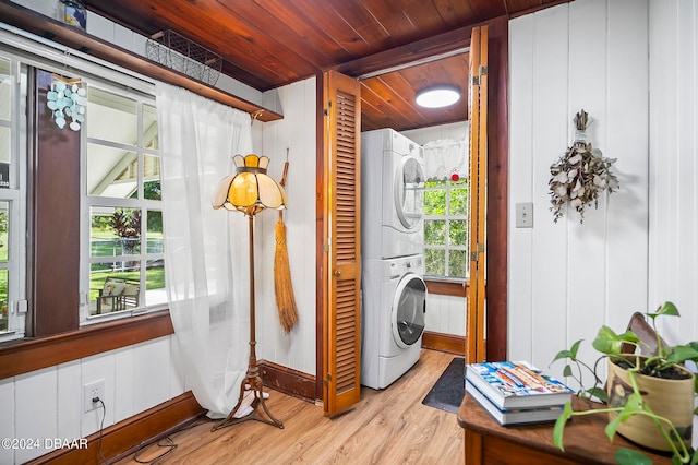 clothes washing area featuring stacked washer and dryer, light hardwood / wood-style flooring, wooden walls, and wooden ceiling