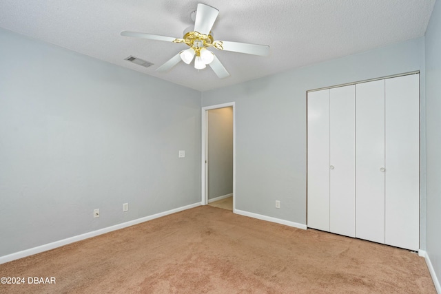 unfurnished bedroom with a textured ceiling, a closet, light colored carpet, and ceiling fan