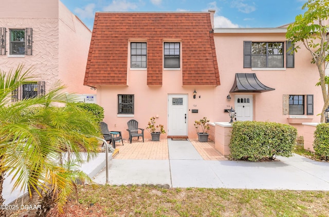 108 Mitchell Pl, Daytona Beach, FL 32118 - view of front of home featuring stucco siding, a shingled roof, a patio area, and mansard roof