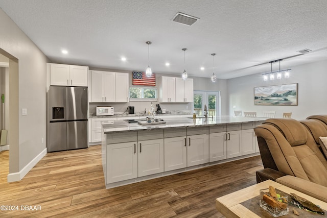 kitchen featuring hanging light fixtures, stainless steel fridge with ice dispenser, and an island with sink