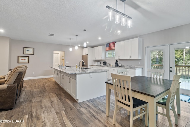 kitchen with french doors, white cabinetry, hanging light fixtures, hardwood / wood-style floors, and an island with sink