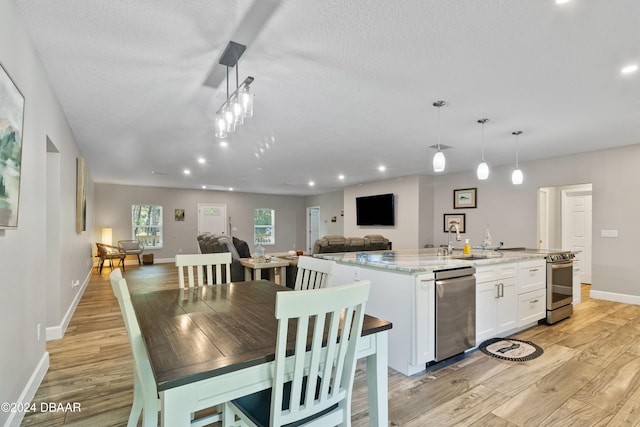 kitchen with stainless steel appliances, white cabinetry, a textured ceiling, hanging light fixtures, and light hardwood / wood-style floors