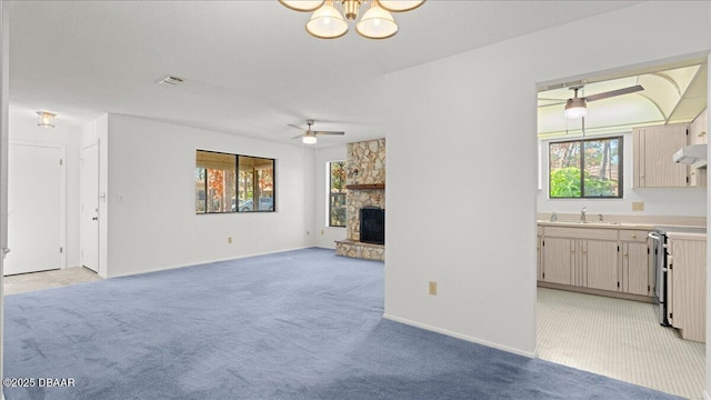 unfurnished living room with light carpet, sink, ceiling fan with notable chandelier, and a fireplace