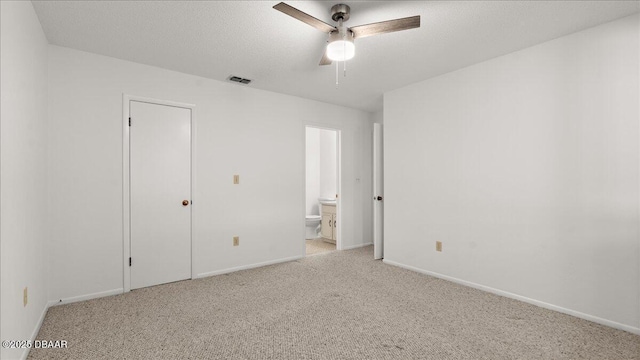 unfurnished bedroom with ceiling fan, ensuite bathroom, light carpet, and a textured ceiling