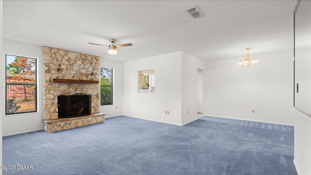 unfurnished living room featuring a stone fireplace, carpet floors, ceiling fan with notable chandelier, and a textured ceiling