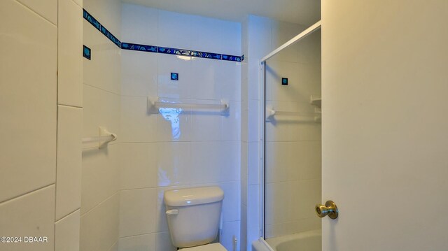 bathroom featuring toilet, shower / bath combination with glass door, and tile walls