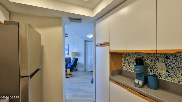 kitchen featuring stainless steel fridge, wood-type flooring, white cabinetry, and backsplash