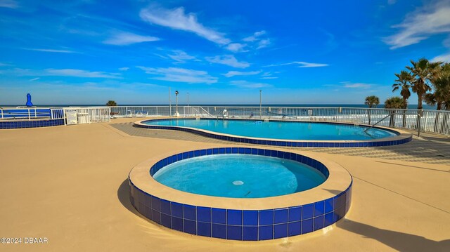 view of pool featuring a water view, a patio, and a hot tub