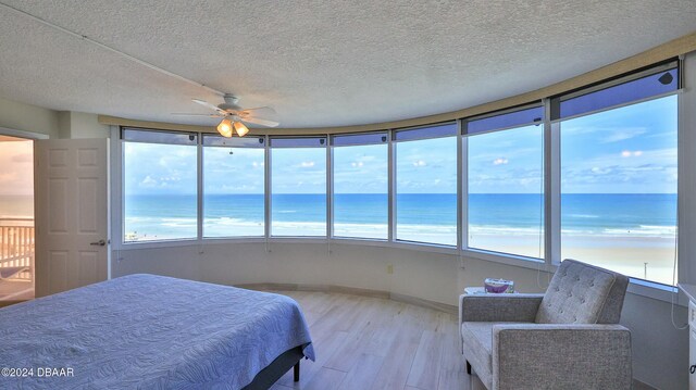 bedroom with ceiling fan, a water view, light hardwood / wood-style floors, and a textured ceiling