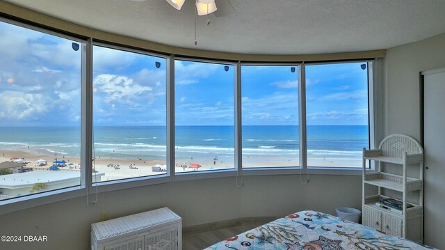 bedroom featuring hardwood / wood-style floors, a water view, ceiling fan, a beach view, and a textured ceiling