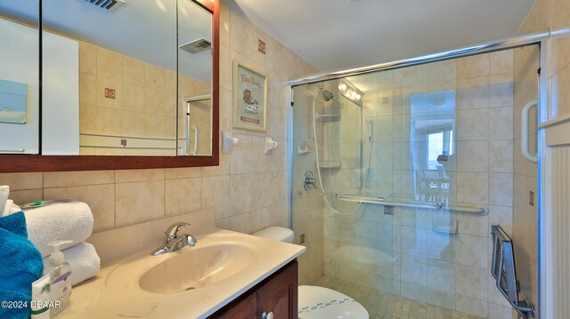 bathroom featuring a shower with door, vanity, tile walls, and toilet