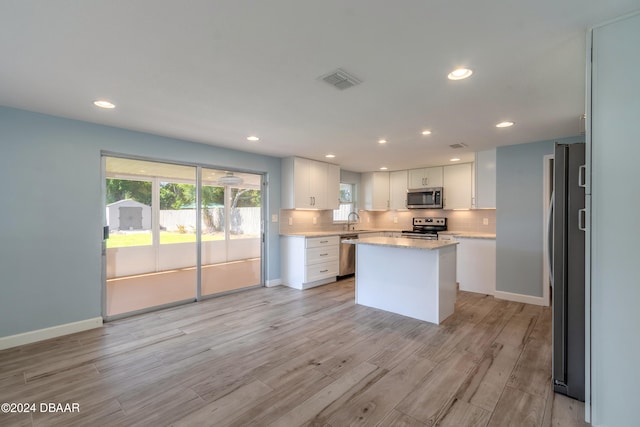 kitchen with stainless steel appliances, light wood-type flooring, light stone countertops, white cabinets, and a center island