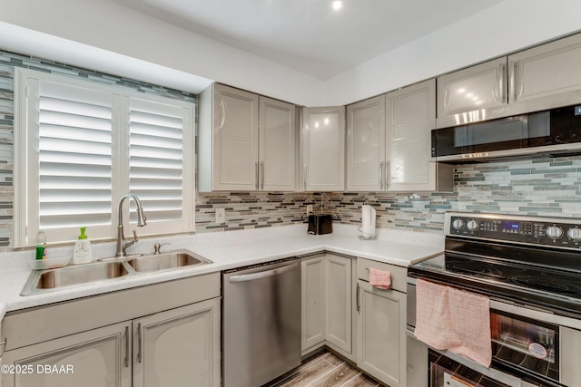 kitchen featuring appliances with stainless steel finishes, sink, backsplash, and gray cabinetry