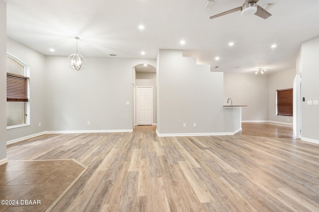 unfurnished living room with ceiling fan with notable chandelier, sink, and light hardwood / wood-style flooring