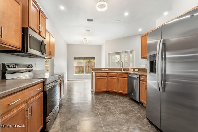 kitchen featuring dark tile patterned floors, kitchen peninsula, appliances with stainless steel finishes, and sink